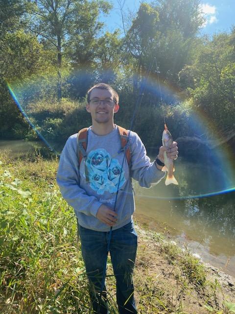 Bryce Griffin smiling while holding a fishing rod and a fish outdoors